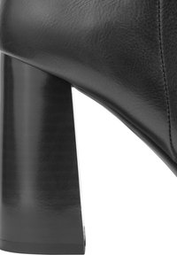 Botte à talon haut en cuir noir avec un large talon carré brillant et des accents cousus le long du bord supérieur. Texture lisse sur toute la surface.