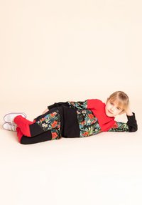 Dwuczęściowy strój składający się z czerwonej bluzki i czarnych spodni w kwiatowy wzór, zaprojektowanych z długimi rękawami i elastycznymi mankietami. Białe trampki.