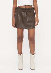 Brauner Leder-Minirock mit doppeltem Schnallen-Gürtel, glatter Textur und streamline Design, kombiniert mit weißen westernähnlichen Stiefeletten.