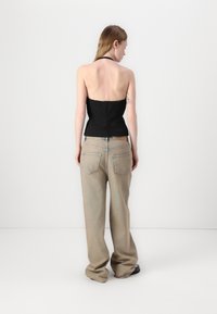 Top nero senza spalline con corpetto aderente, abbinato a jeans beige chiaro a vestibilità ampia con tasche posteriori e un'etichetta in pelle sulla vita.