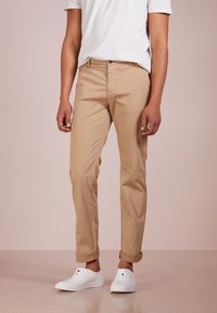 Kaki chinos s úzkým střihem, z bavlněného materiálu, s ohrnutými lemy. Kombinované s bílými teniskami a jednobarevným bílým tričkem.