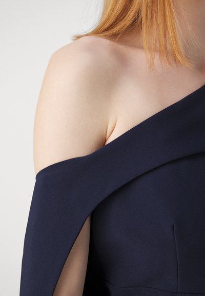 Abito navy a spalla scoperta con scollatura strutturata, caratterizzato da una texture di tessuto liscia e una silhouette aderente, che lascia scoprire la pelle su una spalla.