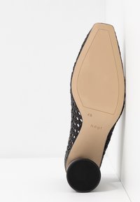 Escarpins noirs tissés avec un bout arrondi, une semelle beige et un talon en caoutchouc texturé. L'étiquette de taille indique 4½.