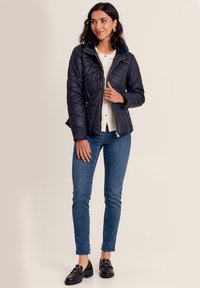 Marineblauer gesteppter Pufferjacke mit einem Kragen aus Kunstpelz, mit Reißverschlusstaschen und einer taillierten Passform, kombiniert mit blauen Skinny Jeans und schwarzen Schuhen.