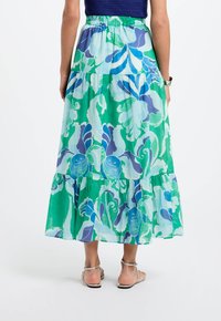 Gonna maxi realizzata in tessuto leggero, con una base verde e motivi floreali blu, vita elasticizzata e design a strati.
