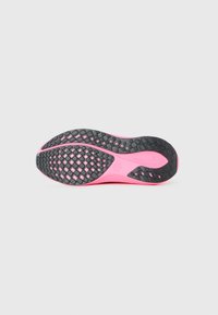 Semelle de chaussure de course en rose avec des motifs de grip texturé en noir et un logo Nike en forme de swoosh au niveau du médio-pied sur un fond gris clair.