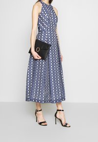 Mörkblå rutmönstrad klänning med figursydd bodice och utsvängd kjol, tillsammans med en svart clutch med ett runt hårdvaruaccent och svarta klackar.