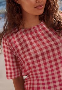 Punavalkoruudullinen lyhythihainen paita, kevyt kangas, pyöreä kaula-aukko ja rakenteeltaan hieman läpikuultava.