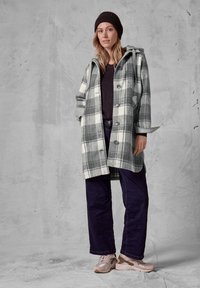 Rutet frakke i grå og hvid, lavet af uldblanding, med hætte, knaplukninger og sidelommer. Kombineret med mørke jeans og lyse sneakers.