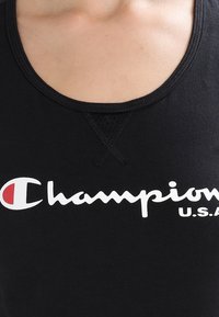 Svart linne med rund halsringning och ärmlös design. Framträdande vitt "Champion"-logga med röd accent ovanför "C."
