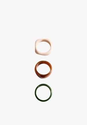 Three rings arranged vertically: a square cream ring, a rounded brown ring, and a green ring. Smooth texture, varied shapes and colors.