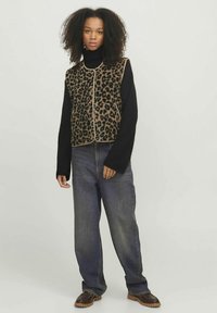 Leopardo rašto liemenė su minkštu tekstūru, smėlio spalvos apdaila, derinama su juodu golfu, laisvo modelio mėlynais džinsais ir rudos spalvos batais.