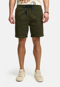 Shorts vert olive avec une taille élastique, un cordon de serrage bleu, des poches latérales et un tissu texturé. Portés avec des baskets de couleur claire.