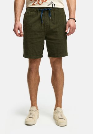 Olive green shorts with an elastic waistband, blue drawstring, side pockets, and a textured fabric. Worn with light-colored sneakers.