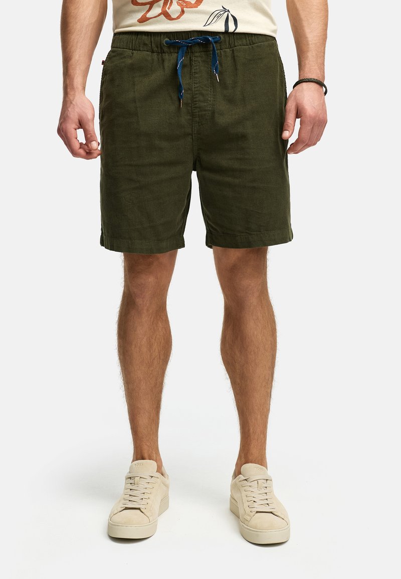 Olive green shorts with an elastic waistband, blue drawstring, side pockets, and a textured fabric. Worn with light-colored sneakers.