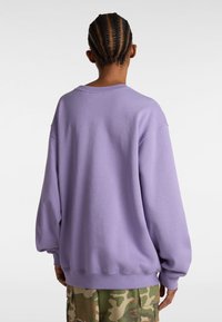 Sudadera de gran tamaño en color lavanda con hombros caídos, cuello de barco acanalado y tejido texturizado, combinada con pantalones de carga de camuflaje.