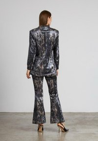 Traje texturizado en negro y plata con pantalones acampanados y una americana ajustada, con un patrón veteado. Zapatos de tacón alto completan el conjunto.
