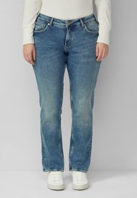 Jasnoniebieskie dżinsy z prostą nogawką, wyposażone w pi�ęć kieszeni, delikatne przetarcia oraz zapięcie na guzik, zestawione z białymi trampkami.