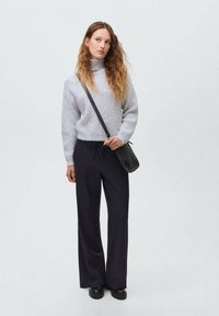 Pulover gri tricotat cu guler înalt, croială lejeră, asociat cu pantaloni largi cu dungi negre. Geantă mică neagră tip crossbody, cizme negre masive.