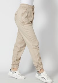 Pantalon beige décontracté avec taille élastique et poches, porté avec des baskets blanches ornées de motifs d'étoiles argentées.