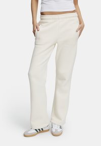 Vita, avslappnade sweatpants med elastisk midja och sidfickor, ihop med flerfärgade sportskor. Slät textur, avslappnad design.