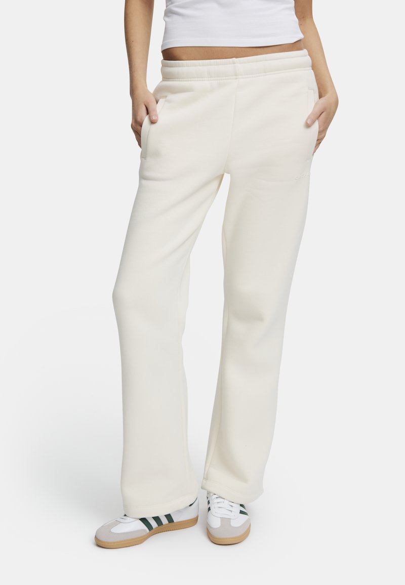 Vita, avslappnade sweatpants med elastisk midja och sidfickor, ihop med flerfärgade sportskor. Slät textur, avslappnad design.