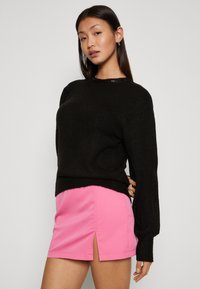 Schwarzer gestrickter Pullover mit langen Ärmeln und strukturiertem Finish, kombiniert mit einem rosa Minirock, der über einen seitlichen Schlitz verfügt.
