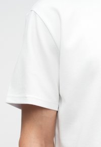 Biała, krótko rękawowa koszulka wykonana z miękkiej mieszanki bawełny. Posiada okrągły dekolt oraz proste, czyste szwy bez widocznych wzorów czy akcentów.