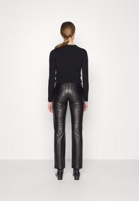 Haut noir à manches longues associé à un pantalon en cuir noir ajusté. L'ensemble présente un design sobre au dos et une coupe droite avec un léger éclat.