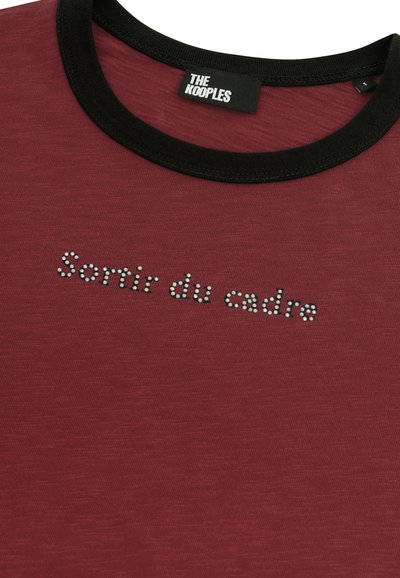 Bordeauxfarbenes T-Shirt mit einem schwarzen Rundhalsausschnitt, versehen mit dem Text "Sortir du cadre", der mit Strasssteinen über die Brust verziert ist.