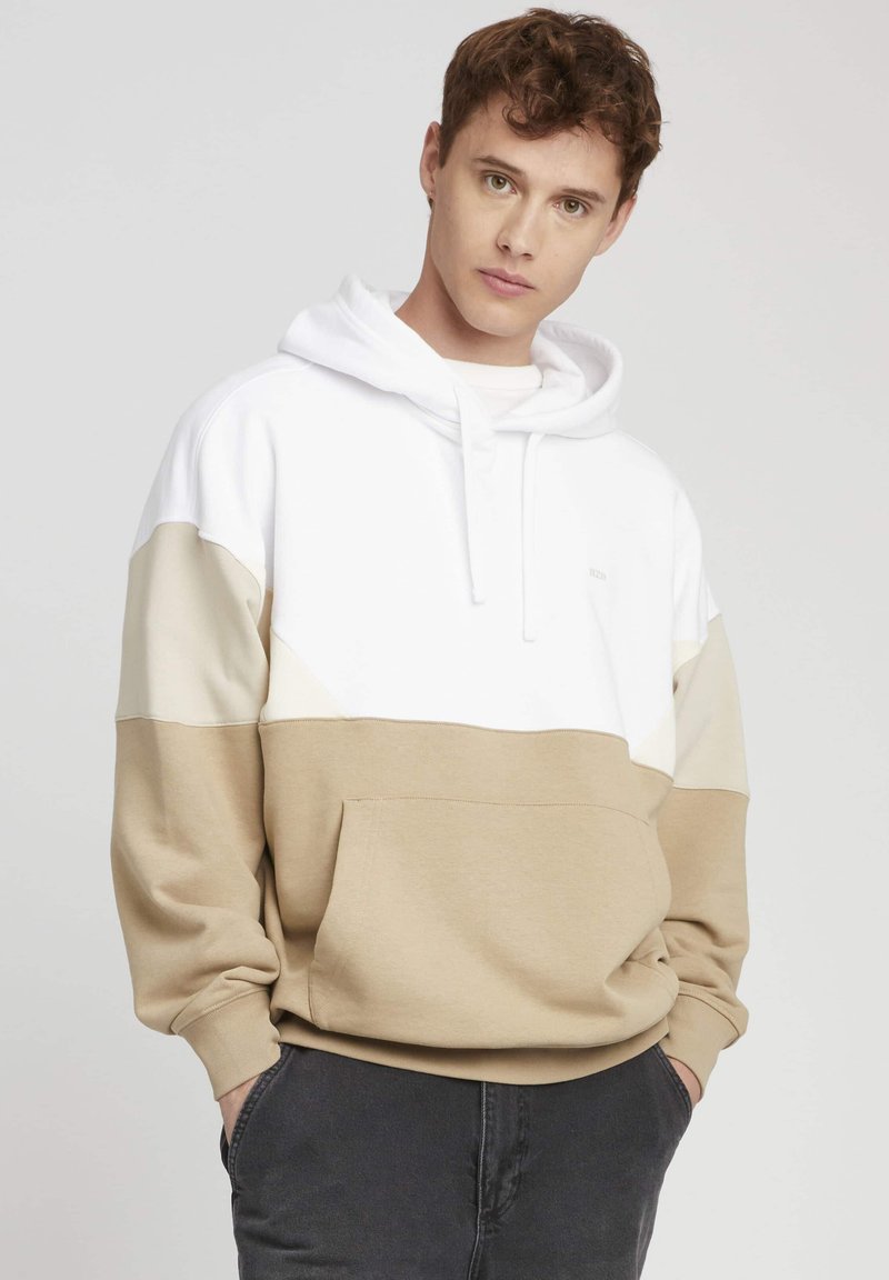 Haut à capuche en coloris beige et blanc, doté d'une poche avant, d'un cordon de serrage pour la capuche et en tissu en coton doux. Coupe décontractée avec des poignets côtelés.