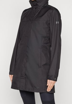 Sort midlængde regnjakke med hætte, sidelommer og trykknapsmanchetter, båret over mørke bukser.