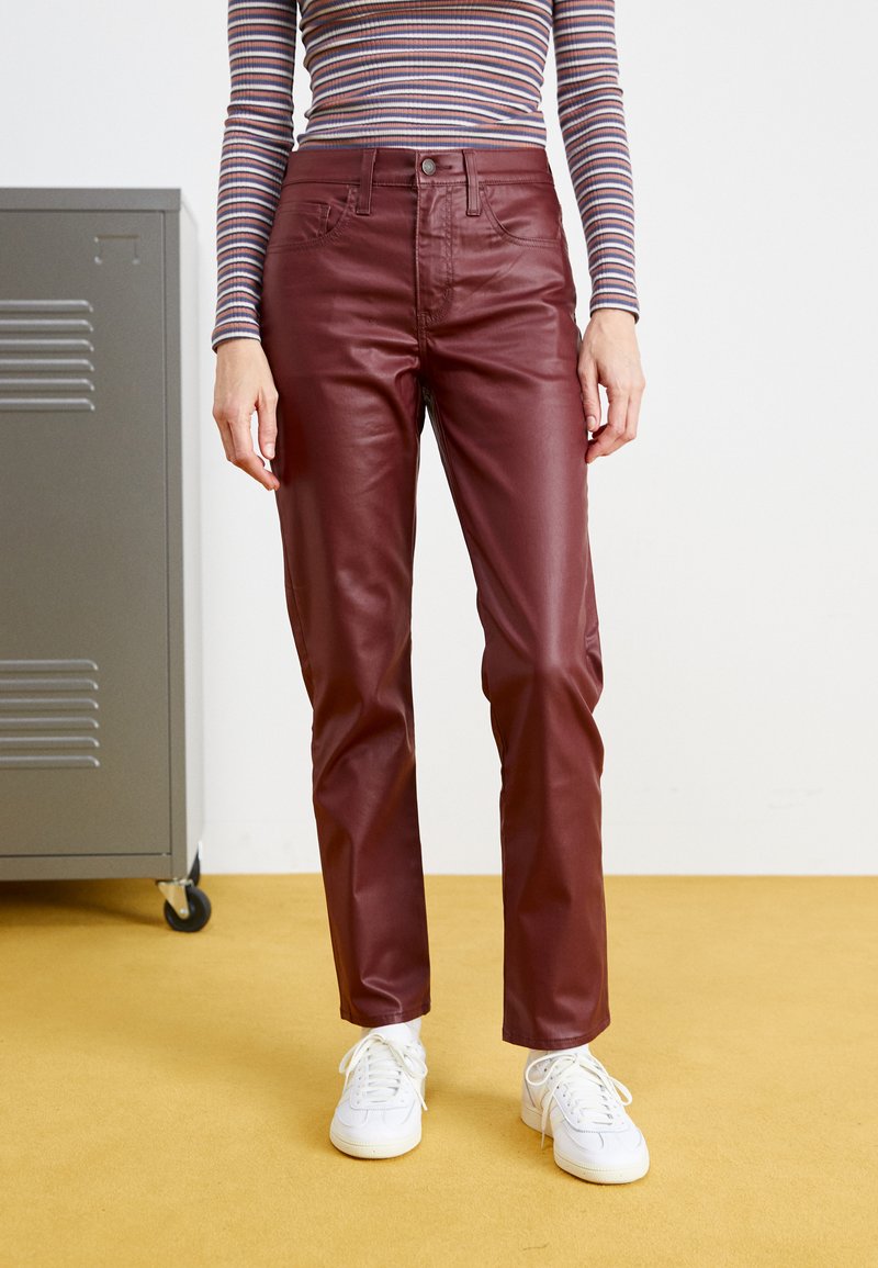 Burgunderfarbene Lederhosen mit Fünf-Taschen-Design, hoher Taille und geradem Schnitt. Getragen mit weißen Sneakers und einem gestreiften Langarmoberteil.