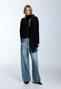 Černý rolák, světlé široké džíny, černý šátek s třásněmi, černé špičaté podpatky, na světlém pozadí.