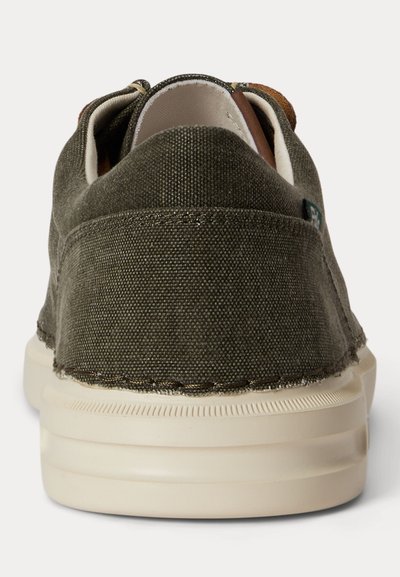 Mørkegrønn lærredssko med hvit gummisåle, sett bakfra.