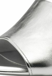 Silverfärgad öppen t�å-slide sandal med en slät, metallisk finish och subtil textur. Har en böjd ovandel och platt sula för enkelt användande.