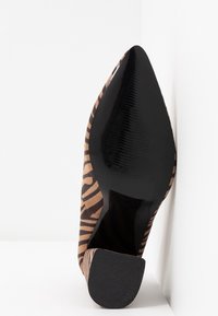 Chaussure à talon haut à bout pointu en daim marron avec des rayures zèbres noires, présentant une semelle extérieure noire brillante et un talon texturé pour une meilleure adhérence.