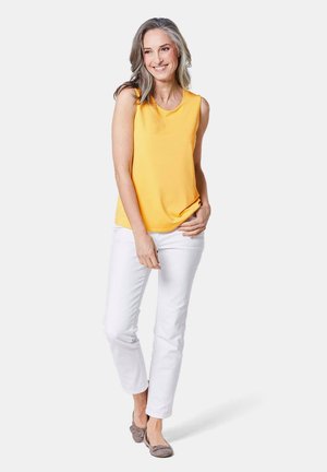 Top giallo senza maniche, tessuto liscio, scollatura rotonda, abbinato a pantaloni in denim bianchi e scarpe piatte grigie con dettaglio a fiocco.