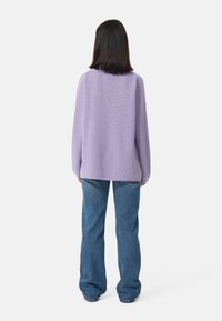 Pull en maille lilas à coupe ample et épaules tombantes, associé à un jean flare bleu. Tissu texturé avec un motif à côtes.