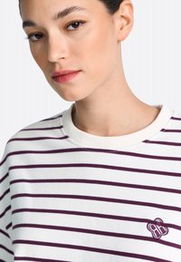 Felpa di cotone bianco con strisce orizzontali color marrone scuro, collo a coste tondo e piccolo logo ricamato sul lato sinistro.