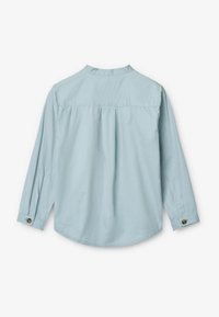Camicia a maniche lunghe azzurro chiaro con orlo arrotondato, dettagli a pieghe sul retro e accenti di bottoni sui polsini. Tessuto morbido.