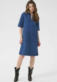 Denim jurk met een kraag, korte mouwen en twee voorzakken. Heeft een losse pasvorm, knielange ontwerp en een donkerblauwe kleur.