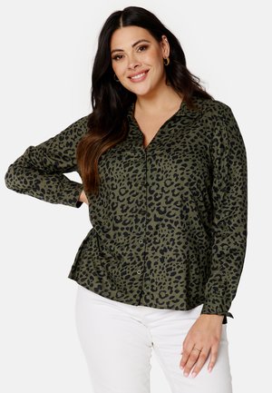 Green button-up shirt with a black leopard print pattern, featuring long sleeves and a relaxed fit, worn with white pants.
