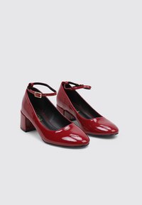 Escarpins en cuir verni rouge avec un bout carré, une bride de cheville et un talon carré. Texture lisse et finition brillante.