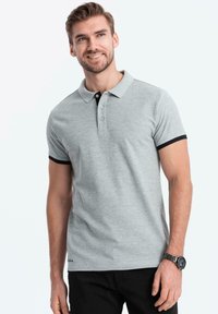 Grijze polo met zwarte kraag en mouwaccenten, drie-knopen sluiting en een aansluitend ontwerp. Gemaakt van een zachte, gestructureerde stof.
