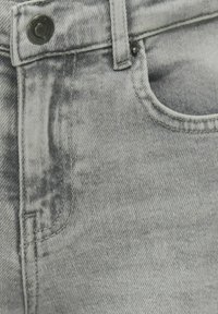 Grå denimjeans med en slittasje finish, som har en forkott lomme, metallknapplukking, og synlige søm detaljer.