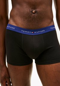 Μαύρα boxer briefs με μπλε μέση που εμφανίζουν το κείμενο "TOMMY HILFIGER" σε λευκό, από μαλακό ύφασμα, σφιχτή εφαρμογή, χωρίς ορατά σχέδια.