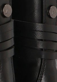 Bota de cuero negra con correas horizontales y herrajes en tono plateado. Textura suave y detalles de costura reforzada visibles.