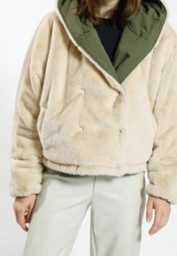 Krämfärgad fuskpälsjacka med en mörkgrön innervante, i en lös passform, med tryckknappar och mjuk textur.