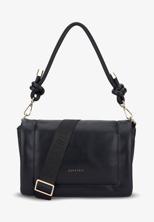 Bolso de hombro negro de cuero con asa acolchada anudada, correa ancha ajustable y logo dorado "EXPATRIÉ" en la solapa frontal.